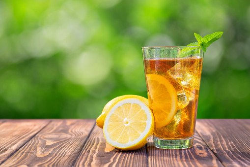 glass of ice tea with mint and lemon on wooden table outdoors