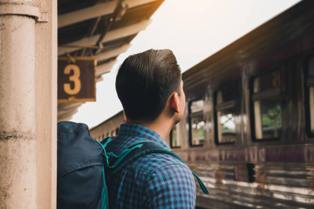 istock Young asian hipster man standing and waiting train on platform. 1154563493