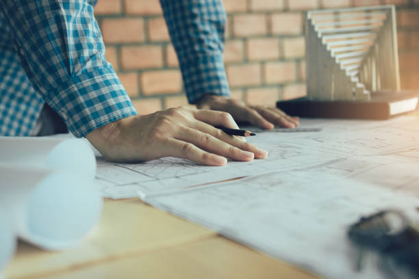 istock Hand of young engineering man drawing on blueprint with model on desk. 1154563775