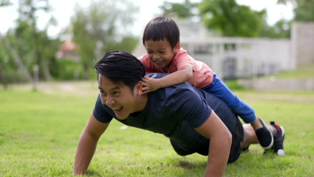 SLO MO Asian father doing push ups with little boy on his back, outdoors.