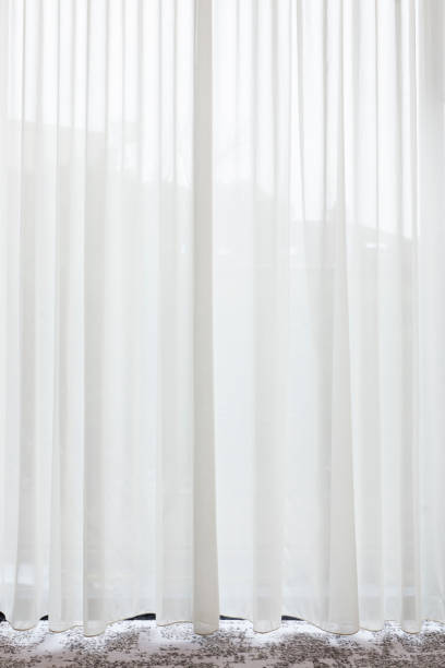 istock Long, white, semy see-through curtain hanging in the window 1154573415