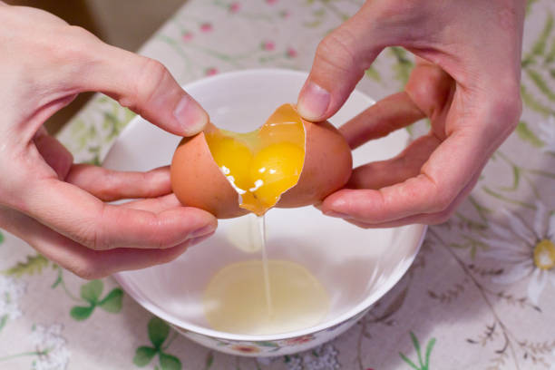 istock Two yolks in one egg. 2 in 1. Women's hands open a unique egg with two yolks. The process of opening eggs for making cake, scrambled eggs, pancakes, muffins. Fashionable ugly food 1154573701