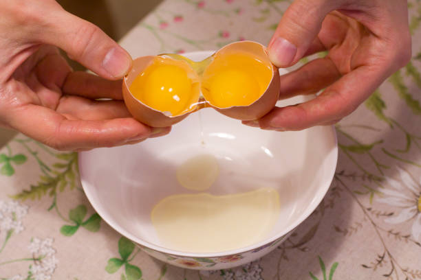 istock Two yolks in one egg. 2 in 1. Women's hands open a unique egg with two yolks. The process of opening eggs for making cake, scrambled eggs, pancakes, muffins. Fashionable ugly food 1154573801