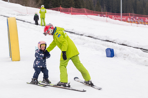 Bukovel, Ukraine - March 13, 2019: A little girl learns to ski at a ski school. The instructor teaches the child to ski. Ski school in the resort town of Bukovel. Bukovel is located in the western Ukraine in the Carpathians.
