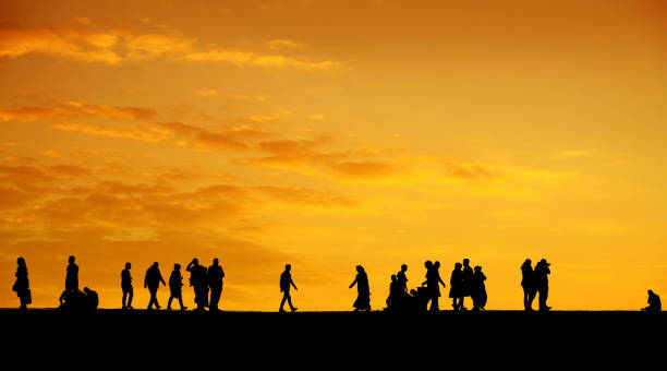istock Silhouetted people walking over orange colored sunset sky 1154580132