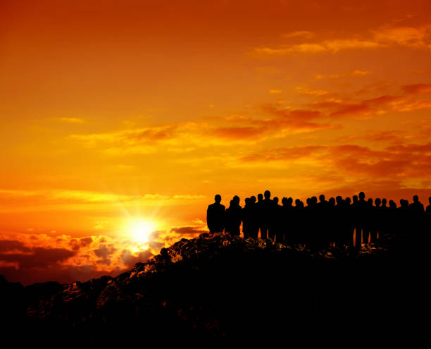 group of silhouetted people on hill watching view over orange colored sunset sky
