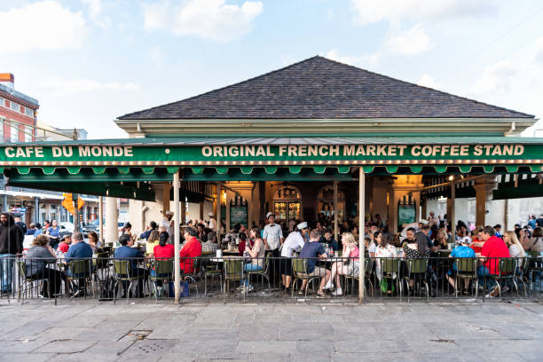 People sitting at tables at iconic Cafe Du Monde restaurant sign eating beignet powdered sugar donuts and chicory coffee New Orleans, USA - April 22, 2018: People sitting at tables at iconic Cafe Du Monde restaurant sign eating beignet powdered sugar donuts and chicory coffee beignet stock pictures, royalty-free photos & images