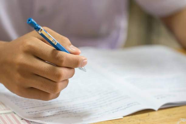 istock Education test concept : Hands Asian students Thai uniform holding pen for testing exams writing answer sheet or exercise for taking fill in exam paper on row wood table at classroom in high school 1154589212