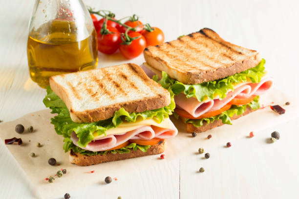 close-up photo of a club sandwich. sandwich with meat, prosciutto, salami, salad, vegetables, lettuce, tomato, onion and mustard on a fresh sliced rye bread on wooden background. olives background. - sandwich club sandwich ham turkey imagens e fotografias de stock