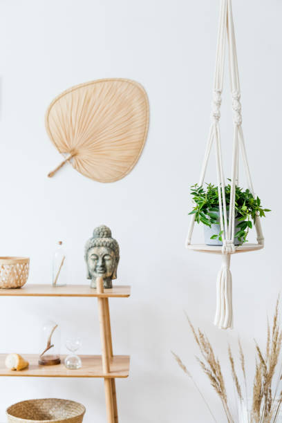 istock Stylish and minimalistic boho interior with design and handmade macrame shelf planter hanger for indoor plants, wooden furnitures, elegant accessories ,rattan basket and leaf. Cozy home decor. 1154596851