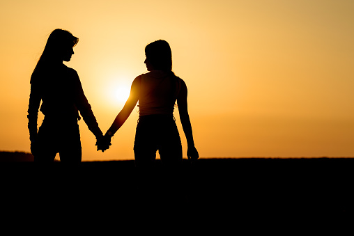 Silhouette two girl holding hand and walking in sunset. Young women on the beach. Lesbian couple near sea.