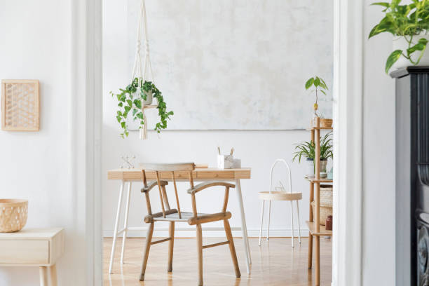 Craft macrame shelf planter hanger for indoor plants, rattan shelf, furnitures and elegant accessories. Cozy home decor. Stylish and minimalistic boho interior of living room. elegante y boho hogar interior de la sala de estar con escritorio de madera, silla y estante. diseño y accesorios elegantes. botánica decoración del hogar con una gran cantidad de plantas y soporte de plantas. pintura abstracta en la pared.