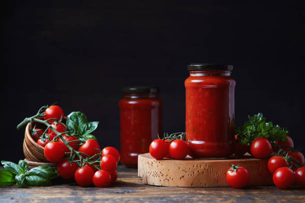 томатный соус в стеклянной банке, помидоры и травы на его стороне. - tomato sauce jar стоковые фото и изображения