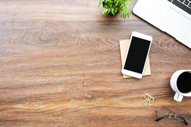 istock Wood office desk table with smartphone with blank mock up screen, laptop computer, cup of coffee and supplies. Top view with copy space, flat lay. 1154604566
