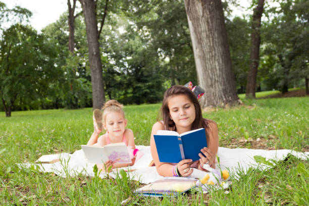 istock Little girls reading books while relaxing on blanket in nature. 1154606429