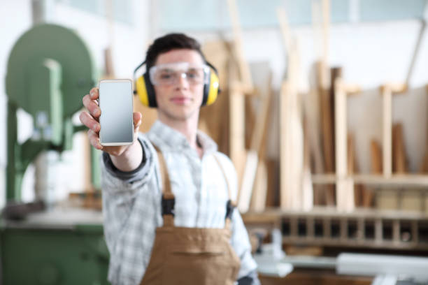istock carpenter man show the mobile phone isolated on carpentry background 1154617400