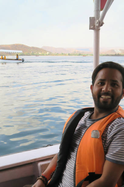 image de passager indien hindou heureux dans le bateau de croisière touristique portant le gilet de sauvetage, la vie orange veste flottabilité aide lac pichola, par taj lake palace, lac pichola udaipur, touriste bateau homme souriant, vacances d’été - motorboating sailing life jacket lake photos et images de collection