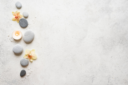 Spa concept on white stone background, tropical flowers, candle and zen like grey stones, top view, copy space.