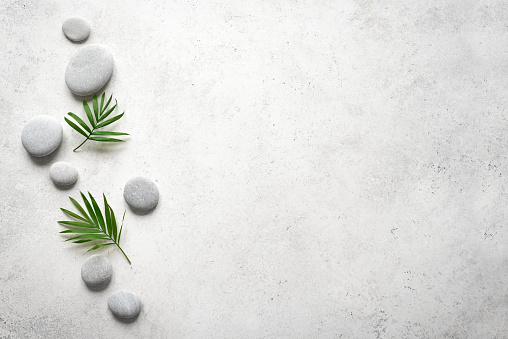 Spa concept on white stone background, palm leaves and zen like grey stones, top view, copy space.