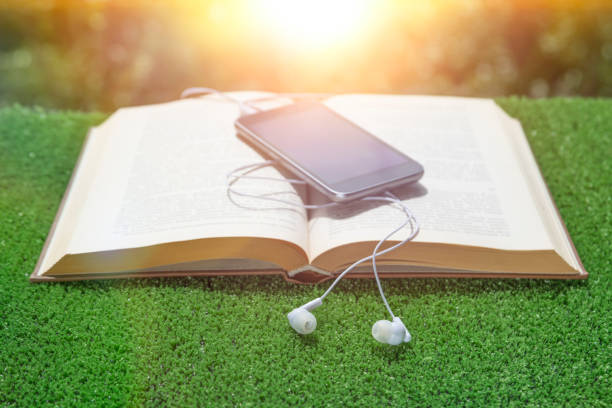istock book, smartphone, headphones on a grass and greenery background. 1154623112