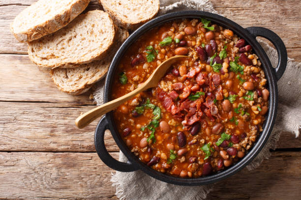 Delicious cowboy stew of beans with ground beef, bacon in a spicy sauce closeup in a bowl. horizontal top view Delicious cowboy stew of beans with ground beef, bacon in a spicy sauce closeup in a bowl on the table. Horizontal top view from above bean stock pictures, royalty-free photos & images