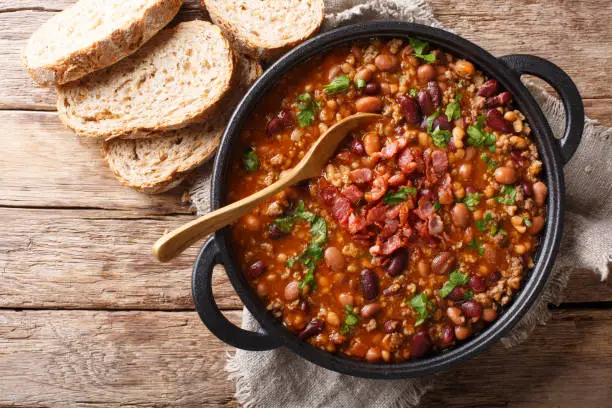 Delicious cowboy stew of beans with ground beef, bacon in a spicy sauce closeup in a bowl on the table. Horizontal top view from above