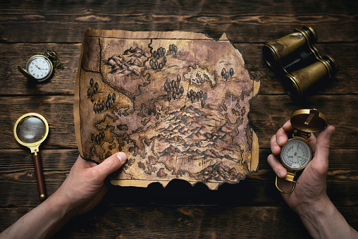 Old map in man adventurer hands on a brown table background. Treasure hunt concept.
