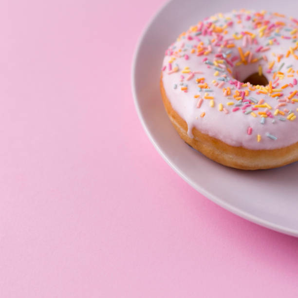 istock Delicious donut with sprinkles on plate at pink table. 1154655407