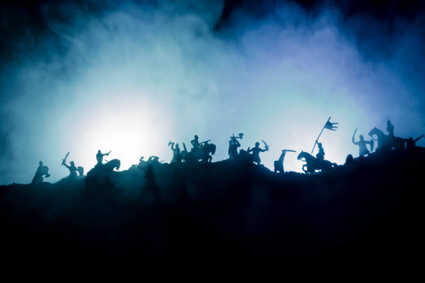 Medieval battle scene with cavalry and infantry. Silhouettes of figures as separate objects, fight between warriors on dark toned foggy background with medieval castle. stock photo