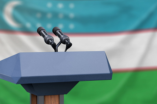 Podium lectern with two microphones and Uzbekistan flag in background