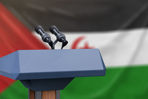 Podium lectern with two microphones and Western Sahara flag in background