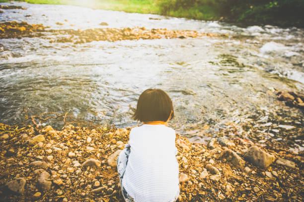 A Asian little girl play on the bank of river, she throw a stone to river.