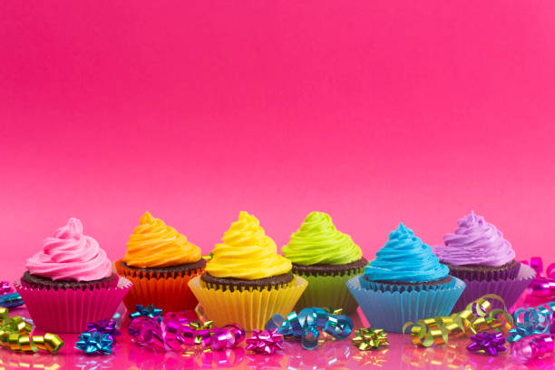 istock Rainbow Colored Frosted Chocolate Cupcakes on a Pink Background 1154695987