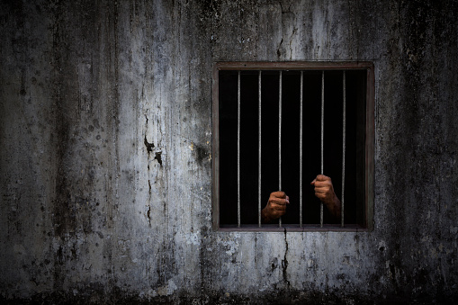 Las manos del prisionero en la barra oxidada de la ventana y la vieja pared de la celda sucia de la prisión photo