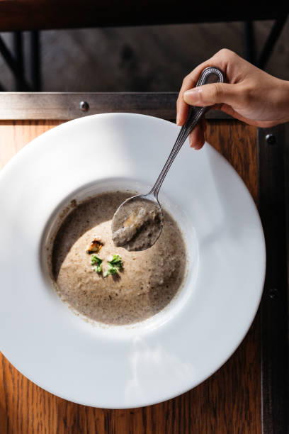 istock Hand scooping mushroom soup with Grouton in white plate with sunlight. 1154720524