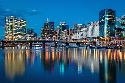 Beautiful illuminated modern Skyscraper Cityscape of Darling Harbour reflecting in the tranquil harbor waters. Pyrmont Bridge, Darling Harbor, Sydney, New South Wales, Australia.