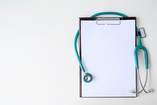 Blank medical clipboard with stethoscope on white background. Copy space.