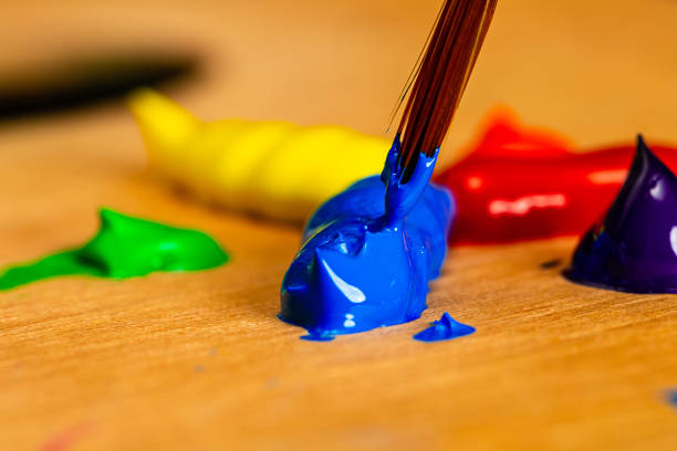 istock Sharp macro of An Artist's paint brush being loaded with blue acrylic paint from blobs of paint on a palette in a primary and secondary color wheel. 1154722704