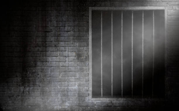 Feixe luminoso com fumo no indicador da prisão com barras oxidadas e parede de pilha velha da prisão do tijolo - foto de acervo