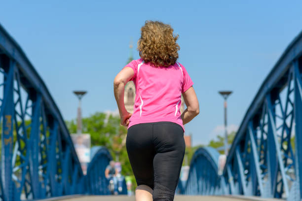 vista posteriore di una donna in forma che fa jogging attraverso un ponte - women rear view one person arch foto e immagini stock