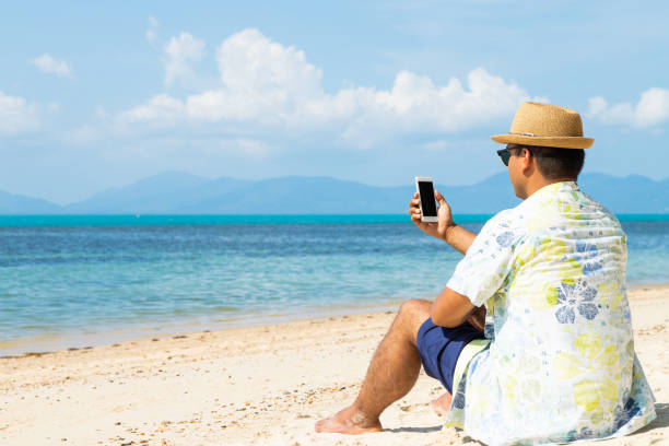 istock Young asian man on the beach using smartphone. 1154733081