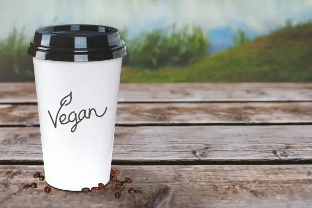 Vegan coffee to-go cup on a rustic wooden table. Nature background and wallpaper. Easy to customize.