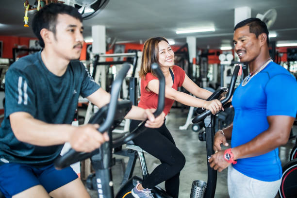 istock Personal trainer coaching two people on bycicle in the gym 1154736481