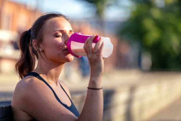Woman drinking protein shake A young woman is sitting outdoors in work out clothes. She is holding a protein shake. protein stock pictures, royalty-free photos & images