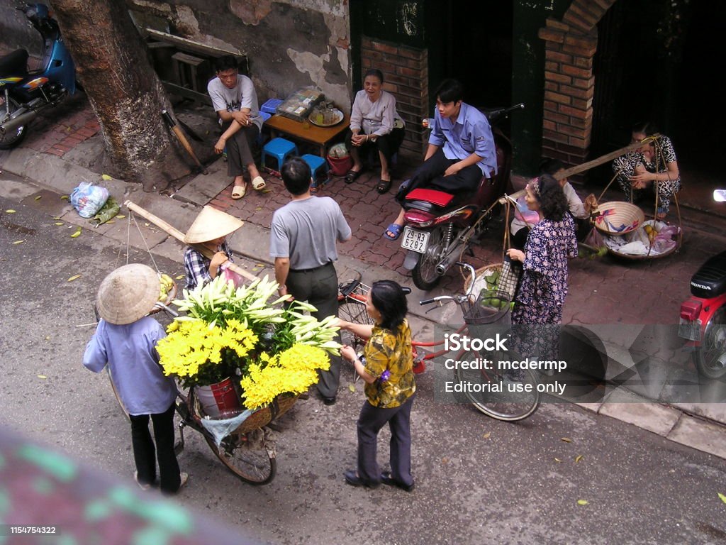 The Flowers are Fresh Today July 6th 2003, Hanoi city centre, Vietnam.  Hanoi is an extraordinary place where you never need go out to shop as venders selling everything from fruit and flowers to magazines, constntly pass by wherever you happen to be staying or eating.  In this picture a woman can be seen buying some bright flowers from a passing street vendor. Adult Stock Photo