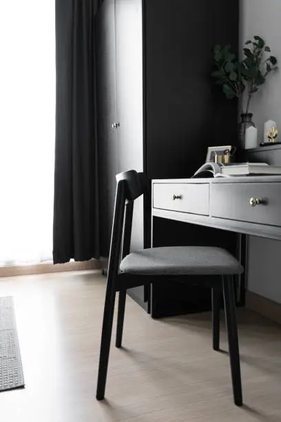Photo of Dressing table corner with black wood power table and black wooden chair  and circular black mirror in natural light scene / cozy interior concept / black interior scandinavian style /interior design