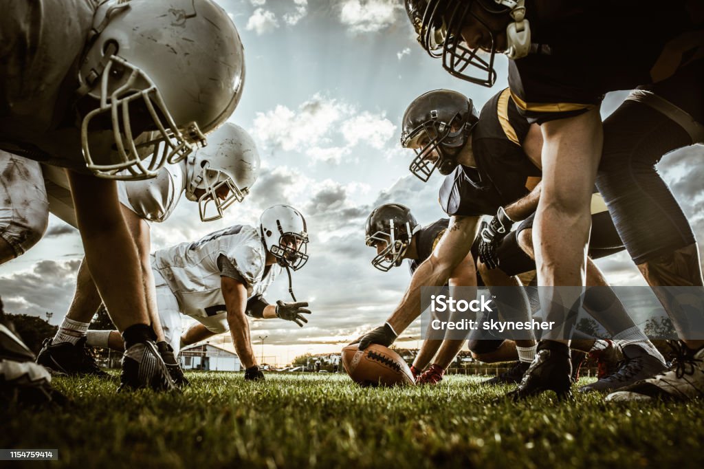 Below view of American football players on a beginning of the match. Low angle view of American football players confronting before the beginning of a match. American Football - Sport Stock Photo