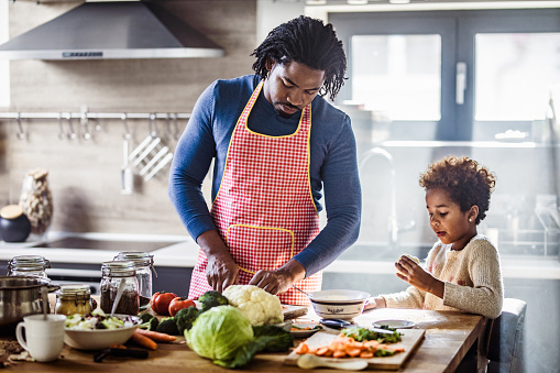 African American single father cooperating with his small daughter while preparing a meal in the kitchen.