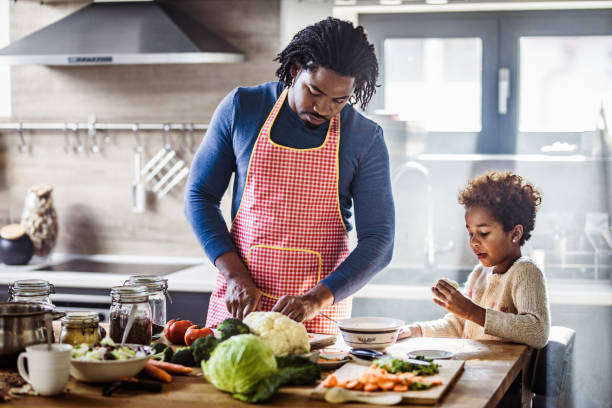 Black father and daughter preparing healthy lunch in the kitchen. African American single father cooperating with his small daughter while preparing a meal in the kitchen. family dinners and cooking stock pictures, royalty-free photos & images
