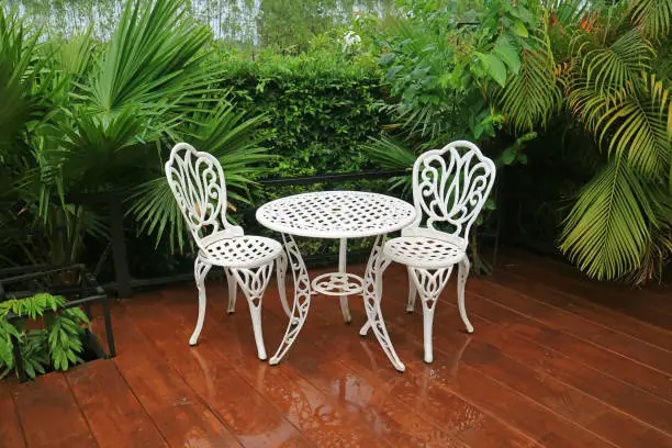 Empty white wrought iron garden tea table and chairs in the patio after rain